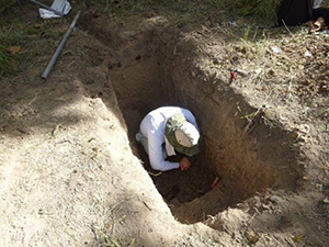 大きな穴の中にしゃがんで土を見る男性の写真