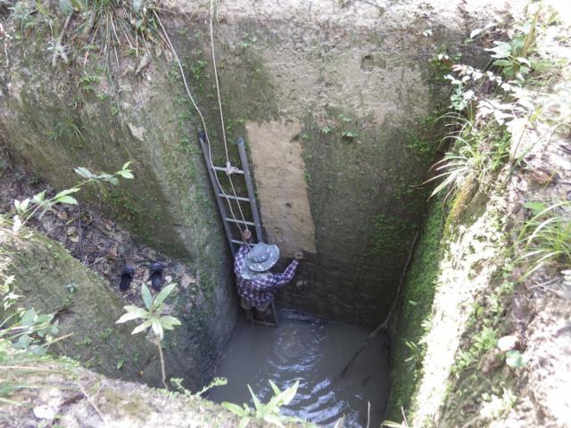 深い穴の底で下半身を水につかりながら穴の壁を調べる人の写真