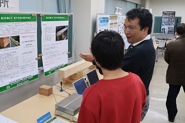 研究成果ポスターの前で内容の説明をする様子の写真