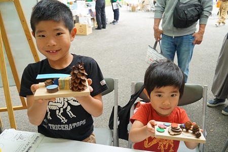 松ぼっくりや端材を使って出来た作品と一緒に写る子供達