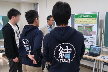 写真02:研究成果ポスターの前で学生さんたちが研究員から説明を聞いている様子