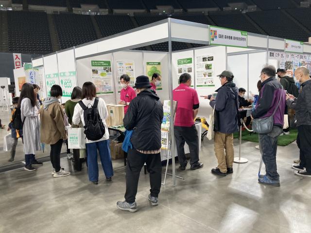 写真右、ブース内で樹木製油に関する研究成果のポスターを展示し、研究者が解説している様子