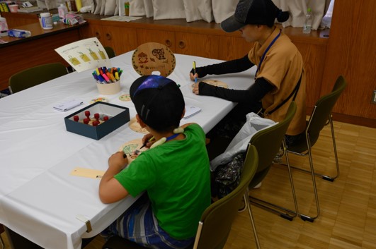 写真6.木製のうちわやしおりに絵を描いている写真